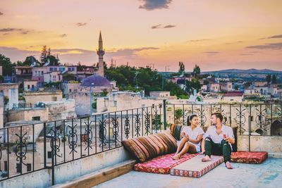 Couple sitting on mattresses in city during sunset