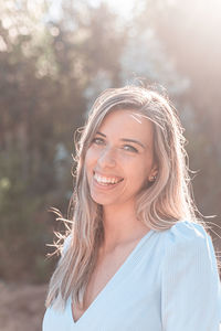 Portrait of smiling young woman standing in forest on sunny day