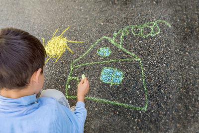 Child draws a house and the sun with chalk on the asphalt. selective focus. paint.