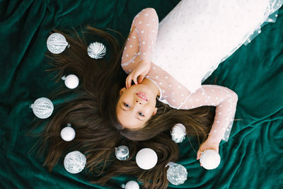 Top view of a girl lying on the floor surrounded by beautiful christmas toys balls