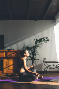 Young caucasian brunette woman practicing yoga at home sitting in lotus pose. vertical format.