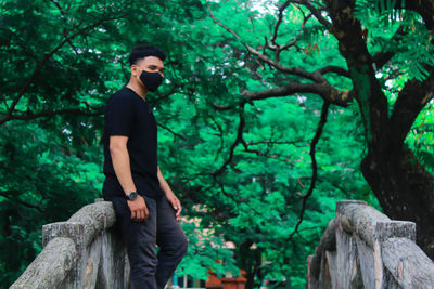 Young man wearing mask standing against tree