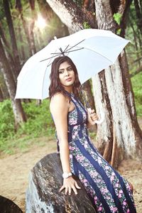 Portrait of young woman against tree trunk in forest