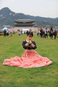 Teenage girl with hands on chin wearing traditional clothing while sitting on grassy field