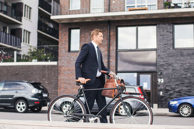 Businessman walking on city street with bicycle against buildings