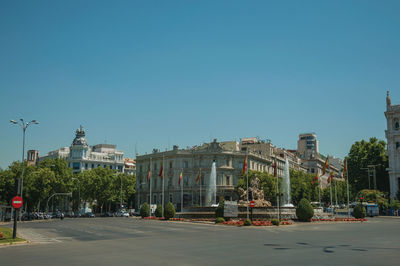 Road by buildings against clear blue sky