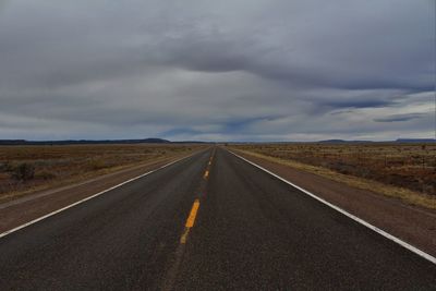 Empty road passing through landscape against cloudy sky