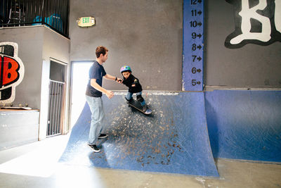 Skateboard instructor holds the hand of student while he is on ramp