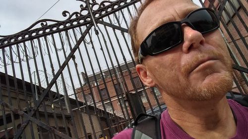 Close-up of mature man wearing sunglasses against closed gate