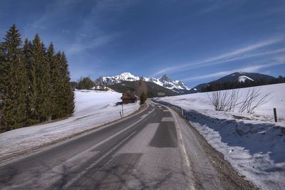 Road by snow covered mountain against sky