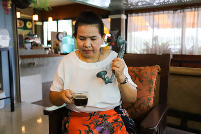 Mid adult woman holding coffee glass and telephone at home
