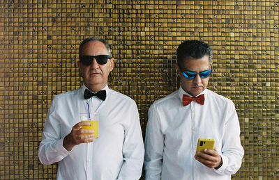 Portrait of a two men standing against yellow brick wall 