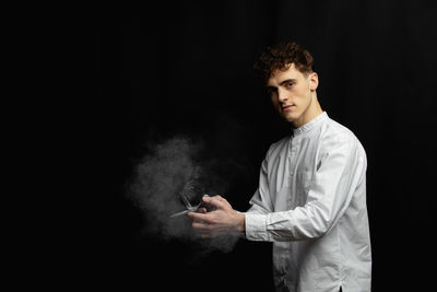 Portrait of young man standing against black background