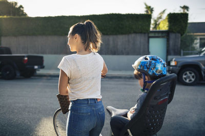 Rear view of woman holding bicycle with son sitting on back seat outdoors