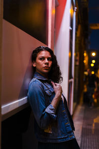 Thoughtful young woman leaning on wall in city at night