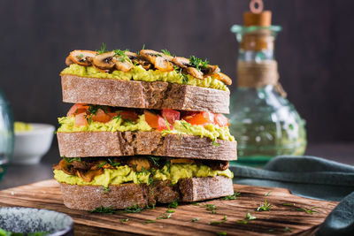 Close-up of a layered rye bread sandwich with guacamole, fried mushrooms, tomatoes and dill