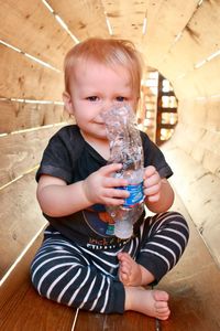 Full length of cute boy holding plastic bottle sitting at playground