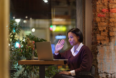 Young friendly afro american woman tutor working remotely in cafe, giving online lesson via laptop