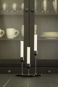 Tree white candles in holders over black dining table - vertical