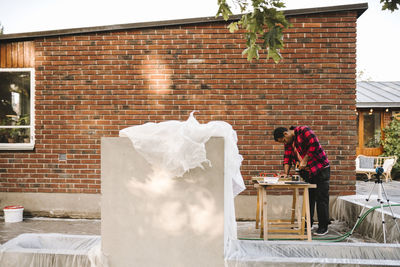 Man using drill machine against brick wall during summer