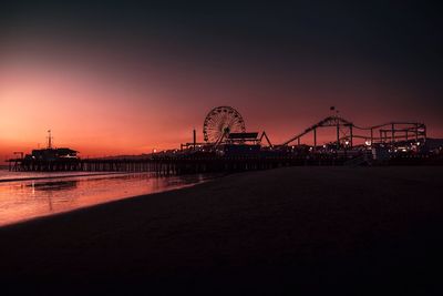 Illuminated ferris wheel by pier against sky at night