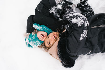 Woman and a child are laying in the snow. mom is smiling and son is making a funny face