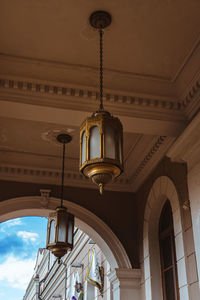 Low angle view of illuminated lamp hanging by building against sky