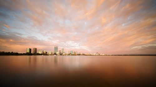 Scenic view of lake by buildings against sky during sunset