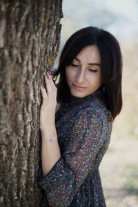 Portrait of beautiful woman standing by tree trunk