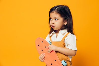 Young woman holding heart shape against yellow background