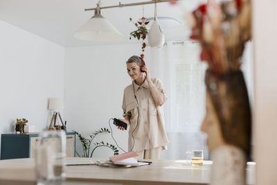 Mature woman wearing headphones listening to music at home