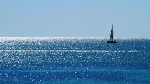 Sailboat sailing in sea against clear blue sky