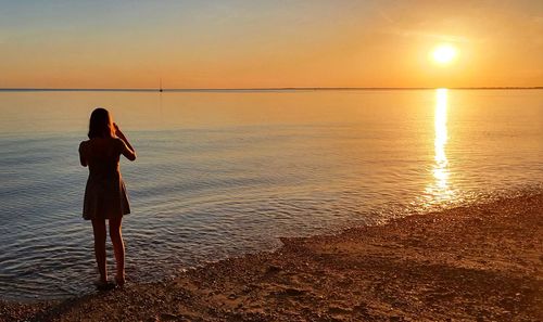 Rear view of teenage girl standing at beach during sunset