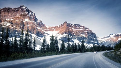 Road amidst snowcapped mountains against sky during winter