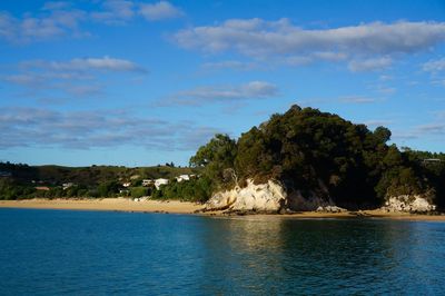 Scenic view of sea, golden beach and green cliff against sky