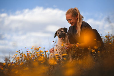 Side view of young woman with dog on field against sky