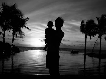 Silhouette people standing by swimming pool against sky during sunset