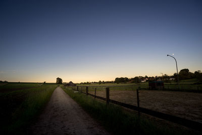 Road amidst field against clear sky during sunset