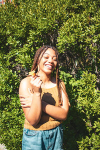 Smiling young woman standing against plants