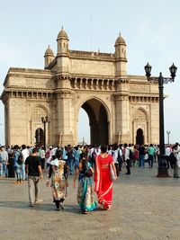 Crowd walking towards gateway to india against sky