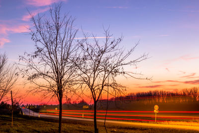 Bare tree by road against sky during sunset