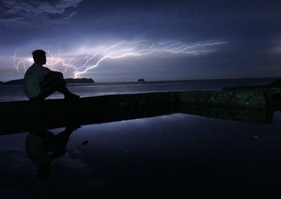 Man sitting by sea against sky at night