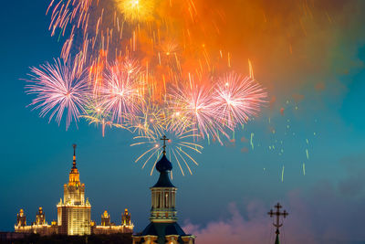 Firework display in illuminated building against sky at night