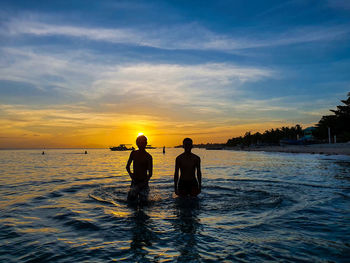 Silhouette men on sea against sky during sunset