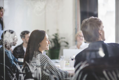 Smiling business people listening while sitting in board room during brainstorming session