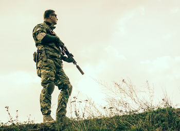 Full length of soldier with rifle standing on field against clear sky
