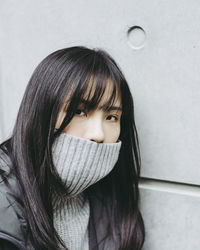 Close-up portrait of young woman covering mouth with turtleneck against wall