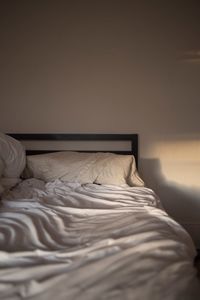 White pillows and crumbled sheet on bed against wall at home