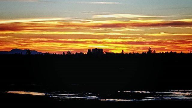 sunset, silhouette, orange color, sky, scenics, beauty in nature, cloud - sky, tranquil scene, idyllic, tranquility, dramatic sky, nature, water, built structure, cloud, moody sky, outdoors, no people, dark, building exterior