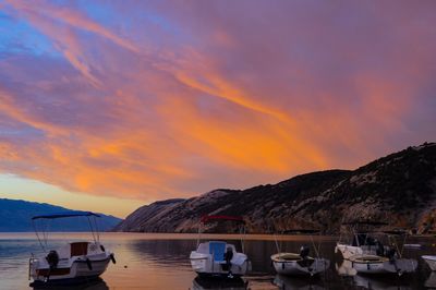 Boats moored on sea against mountains during sunset